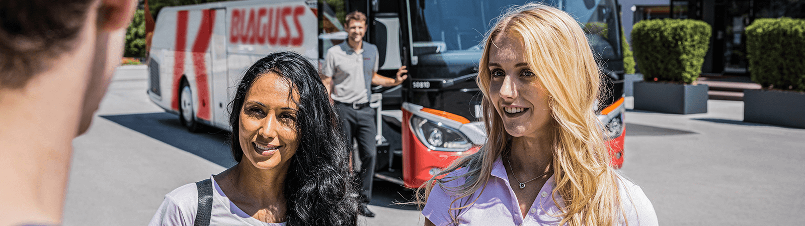 Reisende führen eine Unterhaltung. Im Hintergrund steht ein Lenker und ein Bus.